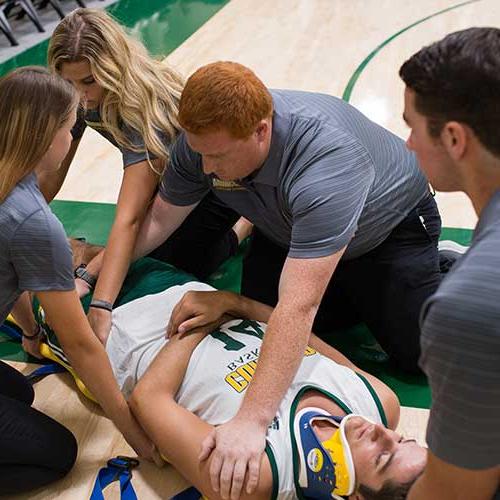 Athletic training students helping an athlete off the court on a backboard.